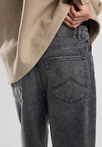 Jeans in denim grigio con vestibilità rilassata, dotati di tasche posteriori e patch in pelle con logo. Il tessuto presenta una texture sbiadita e leggeri segni di usura.