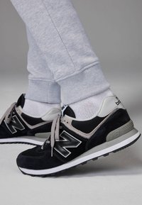 Las zapatillas New Balance en negro y gris presentan una parte superior de ante y malla, cordones redondeados y una suela de goma con un patrón texturizado.