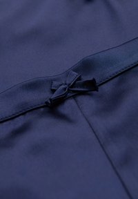 Mörkblått tyg med en slät textur har en liten rosett detalj vid midjan, framhävd av en satinliknande yta.