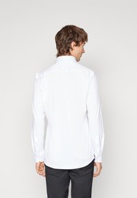 Camicia bianca a maniche lunghe con collo standard, dotata di polsini con bottoni e orlo curvo, realizzata in tessuto morbido.
