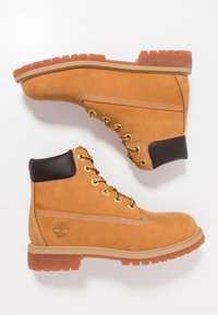 Bottes de travail en suede beige avec bout rond, œillets dorés, accents marron et semelle en caoutchouc crantée. Comprend des coutures visibles et le logo de la marque.