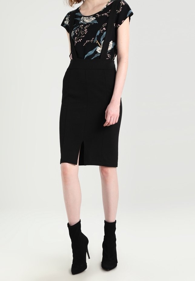 Femme portant une jupe crayon noire taille haute avec une fente à l'avant, un haut noir à manches courtes à motif floral et des bottines noires à talons.