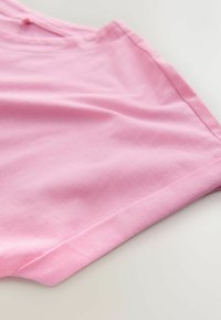 Țesătură din bumbac roz deschis, cu o textură fină; marginea pliată este vizibilă, evidențiind un finisaj curat și o ușoară elasticitate a materialului.