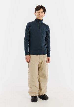 Mornarska dugosleeve pulover s polu-zip ovratnikom, uparen s bež širokim hlačama i crnim cipelama. Mekani materijal i opušteni kroj.