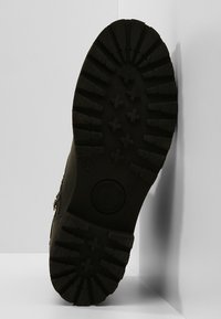 Svart gummisula med djupa mönster och en logo. Klacken har en robust struktur som är utformad för grepp och hållbarhet.