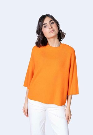 Pullover arancione a maglia con scollatura rotonda ampia, maniche corte e vestibilità comoda, abbinato a pantaloni bianchi su uno sfondo neutro.