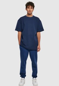 Tengerészkék, oversized póló texturált anyagból, illeszkedő melegítőnadrággal párosítva. A részletek között környak és bordás szegélyek találhatók. Fehér sportcipő.