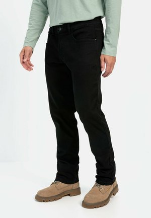 Schwarze Jeans aus Denim mit slim fit, ausgestattet mit einem klassischen Fünf-Taschen-Design und dezenten Steppdetails, getragen mit hellbraunen Stiefeln.