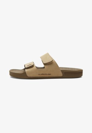 Sandale en cuir marron avec deux sangles Velcro réglables, semelle texturée et semelle en caoutchouc solide. Logo "Quiksilver" imprimé sur le côté.