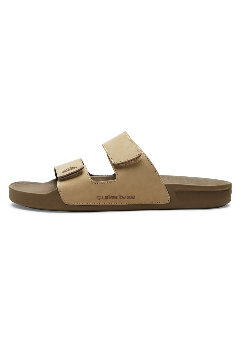 Sandale en cuir marron avec deux sangles Velcro réglables, semelle texturée et semelle en caoutchouc solide. Logo "Quiksilver" imprimé sur le côté.