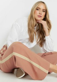 Lichtroze wijde broek met crèmekleurige zijstrepen, gecombineerd met een witte, lange mouw shirt. Glad materiaal, losse pasvorm en subtiele glans.