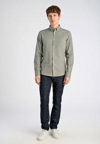Lichtgrijze overhemden met knopen en een zak, gecombineerd met donkere denim jeans en witte sneakers. Gladde textuur; casual pasvorm; lange mouwen.