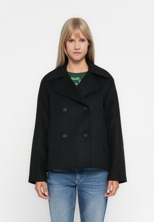 Svarte dobbeltradte peacoat med bred krage, utstyrt med store svarte knapper og en firkantet passform, kombinert med en grønnstripete genser.
