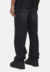 Czarne dżinsy o luźnym kroju, z dwoma tylnymi kieszeniami i lekko przypruszonym kolorem; noszone z czarnymi sportowymi butami.