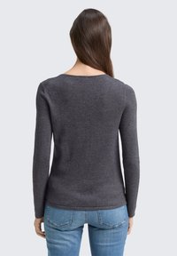 Sötétszürke, hosszú ujjú pulóver, lekerekített nyakkivágással, slim fit fazonnal és sima textúrával, kék farmernadrággal párosítva.