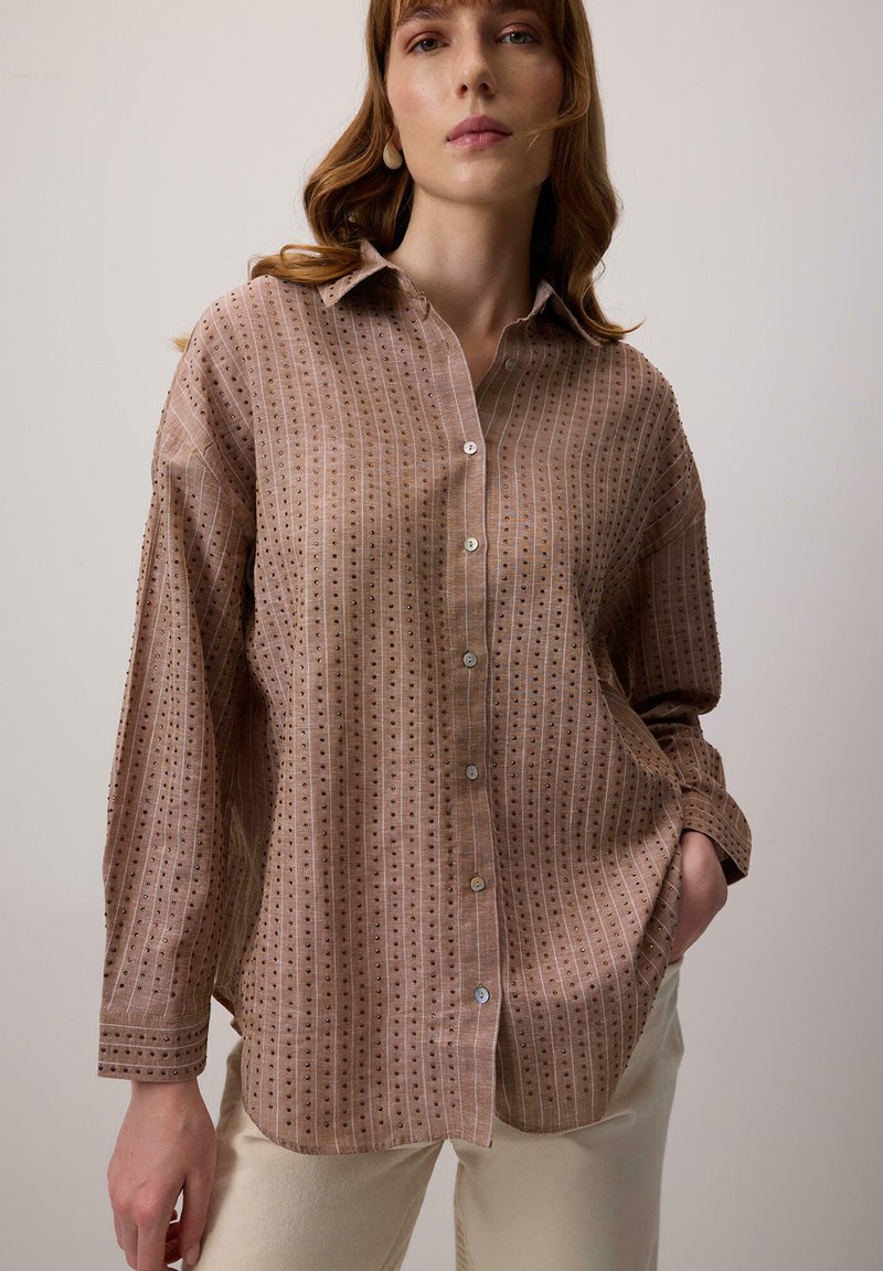 Svetlo rjava srajca z gumbi, z teksturiranim vzorcem in manjšimi izrezi. Ima klasičen ovratnik in dolge rokave, izdelana je iz lahkotnega blaga.