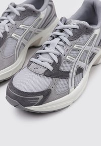 Baskets de sport grises comportant une combinaison de matériaux en mesh et en suède, avec une surface texturée, un bout arrondi et des accents blancs contrastés.
