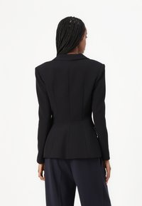 Fekete, struktúrált blézer hegyes hajtókákkal, feszes derékkal és peplum aljjal. Simas texture, hosszú ujjakkal és minimalista dizájnnal.