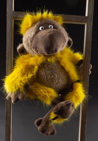 Plush monkey toy with brown and tan fur, bright yellow accents, large round eyes, and stitched mouth. Features soft limbs and a textured body.