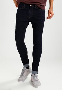 Mörka jeans med slim fit, synlig sömnad, femficksdesign och uppvikt fåll, i kombination med grå sneakers.
