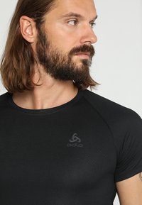 Black fitted athletic shirt with short raglan sleeves, textured fabric, and a subtle logo on the chest. Smooth finish and lightweight design.