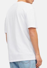 Witte, T-shirt met korte mouwen, ronde halslijn, zachte katoen materiaal, relaxte pasvorm, gezien van achteren, gecombineerd met lichtblauwe denim jeans.