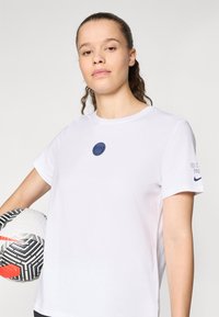 White cotton T-shirt featuring a blue circular logo at the center and "Nike Paris" text on the sleeve, held next to a patterned soccer ball.