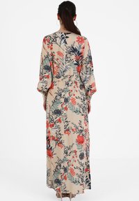 Langes, florales Kleid mit beigefarbenem Hintergrund, roten und marineblauen Blumen sowie grünen Blättern. Hergestellt aus leichtem Stoff, mit weit geschnittenen Ärmeln.