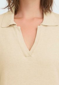 Pullover beige in maglia con scollatura a V e colletto ripiegato. Texture morbida e dettagli a coste fini in tutto il capo.