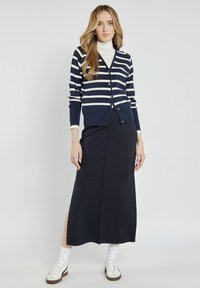 Granatowa i biała sweter w paski z guzikami, zestawiony z granatową długą spódnicą z bocznym rozcięciem i białymi trampkami. Gładka tekstura.