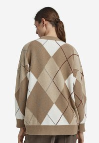 Beżowy sweter w argyle z kremowymi, brązowymi i szarymi rombami. Dzianinowa faktura, luźny krój, ściągacz na dole i mankietach. Widok z tyłu.