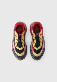 Αθλητικά παπούτσια με πολύχρωμο σχέδιο που περιλαμβάνει τόνους κίτρινου, μαύρου και κόκκινου, λάστιχο σόλα, υφή στο επάνω μέρος και περίπλοκο σύστημα κορδονιών.
