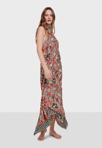 Vestido maxi con un patrón de paisley en rojo, negro y beige. Presenta un cuello alto, un corte holgado y un dobladillo curvado. Hecho de tejido ligero.