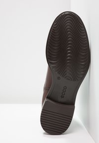 Braunes Leder-Schuhwerk mit einer strukturierten schwarzen Gummisohle, die geschwungene Rillen und Erhöhungen für besseren Halt aufweist. Logo an der Seite angebracht.