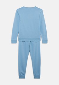 Jasnoniebieski dres składający się z bluzy i spodni w miękkim materiale, z prążkowanymi mankietami oraz małą tylną kieszonką na spodniach.
