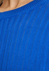 Blauer Strickpullover mit gerippter Textur und chevronartigem Muster. Rundhalsausschnitt und weicher Stoff, der vertikale Linien zeigt.