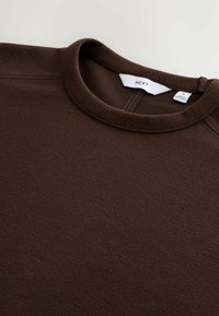Bruine getextureerde sweatshirt met een ronde halslijn en ribgebreide randen. Label toont het merk "NEXT" en maat "M." De stof lijkt zacht en warm te zijn.
