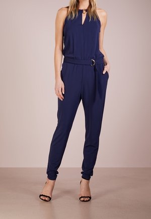 Granatowy kombinezon z odkrytymi ramionami, z dekoltem w kształcie łezki, talią podkreśloną paskiem oraz zwężanymi nogawkami. Lekki materiał o gładkiej strukturze.