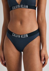Sivi bikini set Calvin Klein, ki vključuje top z V-izrezom in nizko rezane hlačke, oboje z raztegljivim pasom slogom.