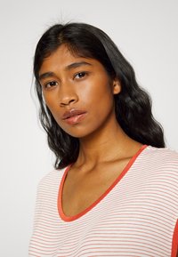 T-shirt às riscas com riscas vermelhas sobre um fundo branco, com um decote amplo e um contorno vermelho contrastante à volta do colarinho.