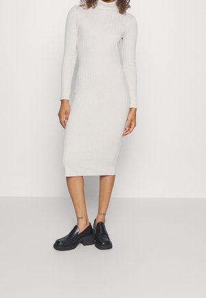 Prążkowana, kremowa sukienka midi z długimi rękawami i stójką. W połączeniu z czarnymi, masywnymi loafersami o gładkiej skórzanej fakturze.