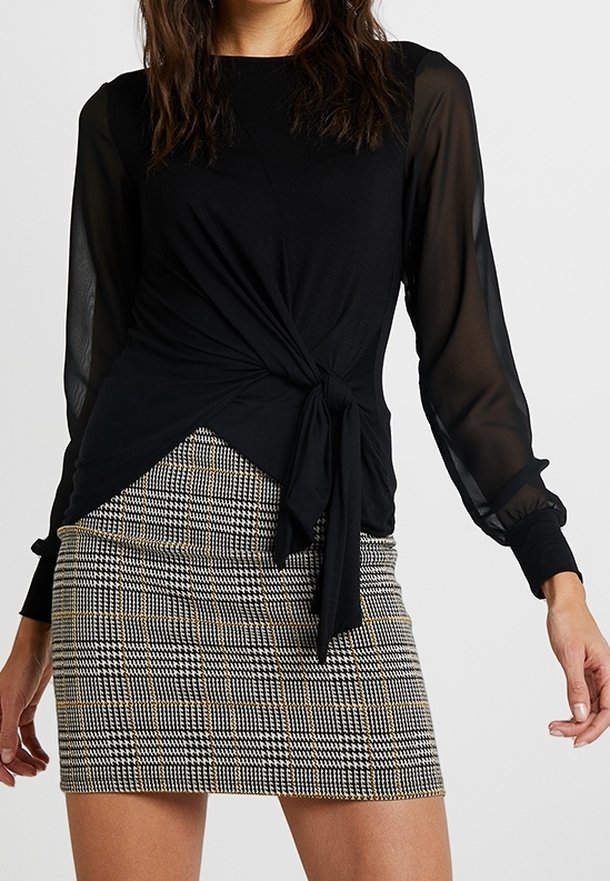 Black long-sleeve top with a knot detail at the waist, paired with a checkered mini skirt featuring black, white, and gold patterns.