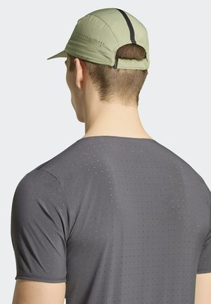 Homme portant une casquette de sport vert clair à l'envers et un maillot de sport gris perforé, vu de dos sur fond uni.
