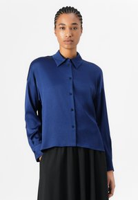 Chemise boutonnière bleu marine en tissu doux, dotée d'un col, de manches longues et d'une coupe droite, accompagnée d'une jupe noire.