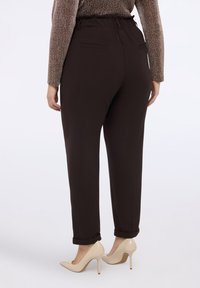 Braune, strukturierte Hose mit elastischem Bund, schlanker Passform und zwei Gesäßtaschen, kombiniert mit nudefarbenen High Heels.