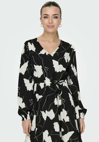 Robe noire avec un motif floral abstrait blanc, décolleté en V, manches longues et ceinture à nouer. Tissu doux avec une texture fluide.