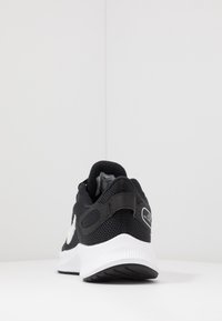 Schwarzer Sportschuh mit Mesh-Obermaterial, weißer Sohle, gepolstertem Schaft und reflektierendem Logodetail an der Ferse. Strukturiertes Profil für besseren Halt.