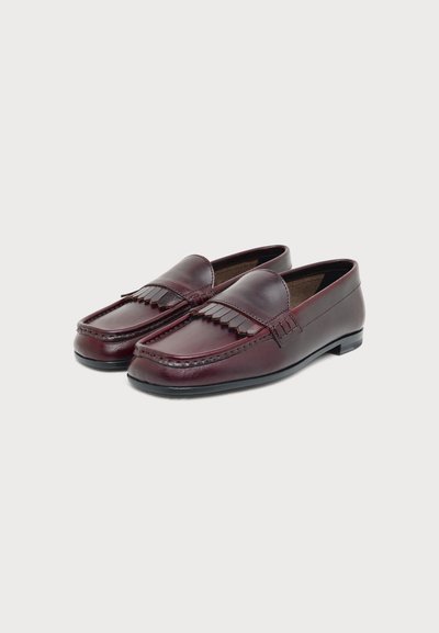 Paire de mocassins en cuir bordeaux foncé avec un détail de franges décoratives à l'avant et des semelles noires, présentée sur un fond clair uni.