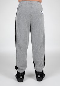 Grijze geribbelde sweatpants met zwarte zijkanten, een elastische tailleband en een merklabel op de achterkant. Gecombineerd met zwarte schoenen met een logo.