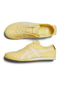 Żółte płócienne trampki z białymi akcentami, niskim profilu, okrągłym noskiem oraz sznurowaniem z wieloma oczkami i wyściełanym kołnierzem.